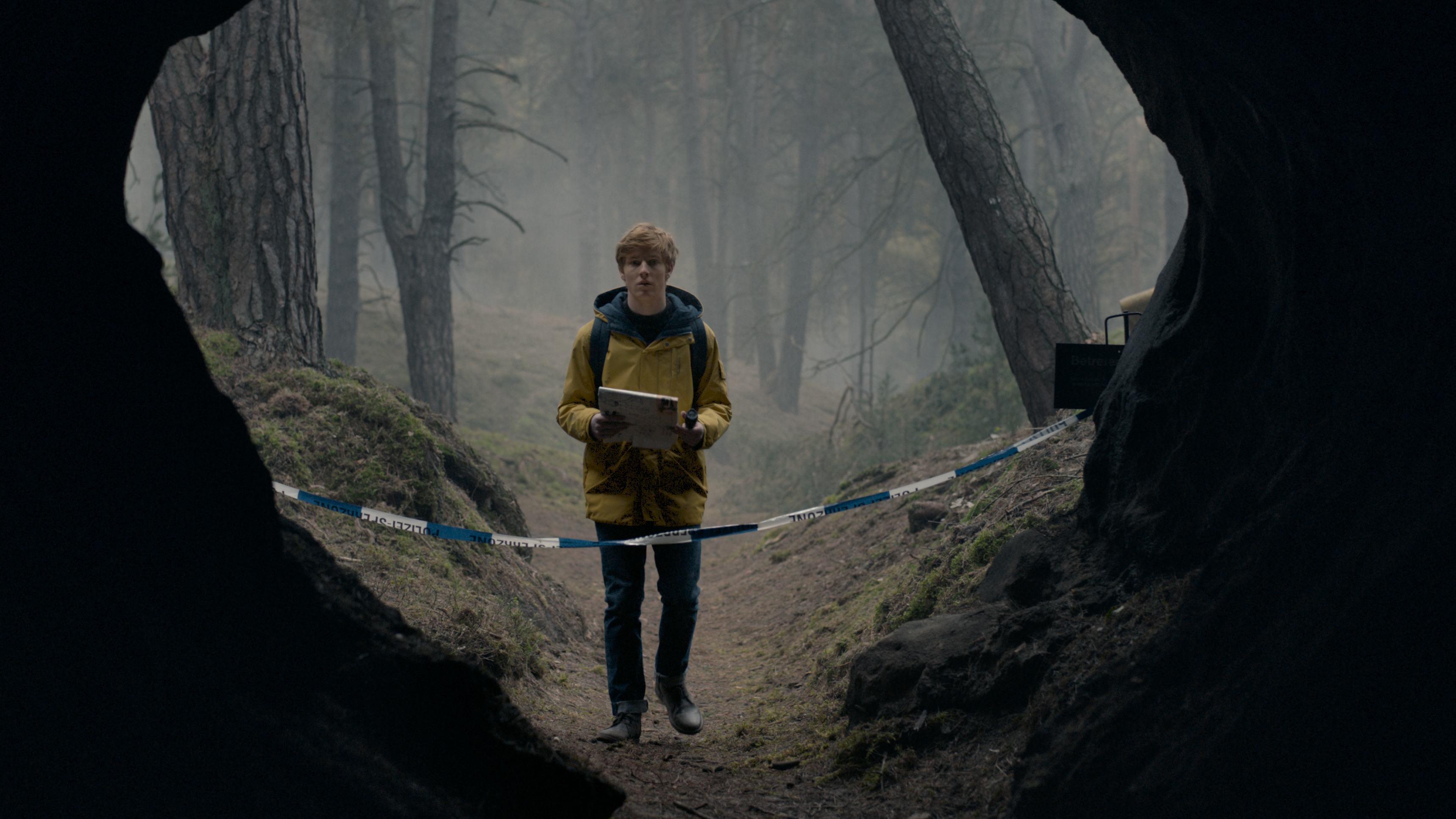 Jonas Kahnwald (Louis Hofmann) peers into a cave that's been blocked off by caution tape in Netflix's Dark.