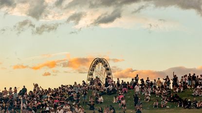 Crowds at Coachella 2026 sat on a hill at dusk, with a ferris wheel in the background
