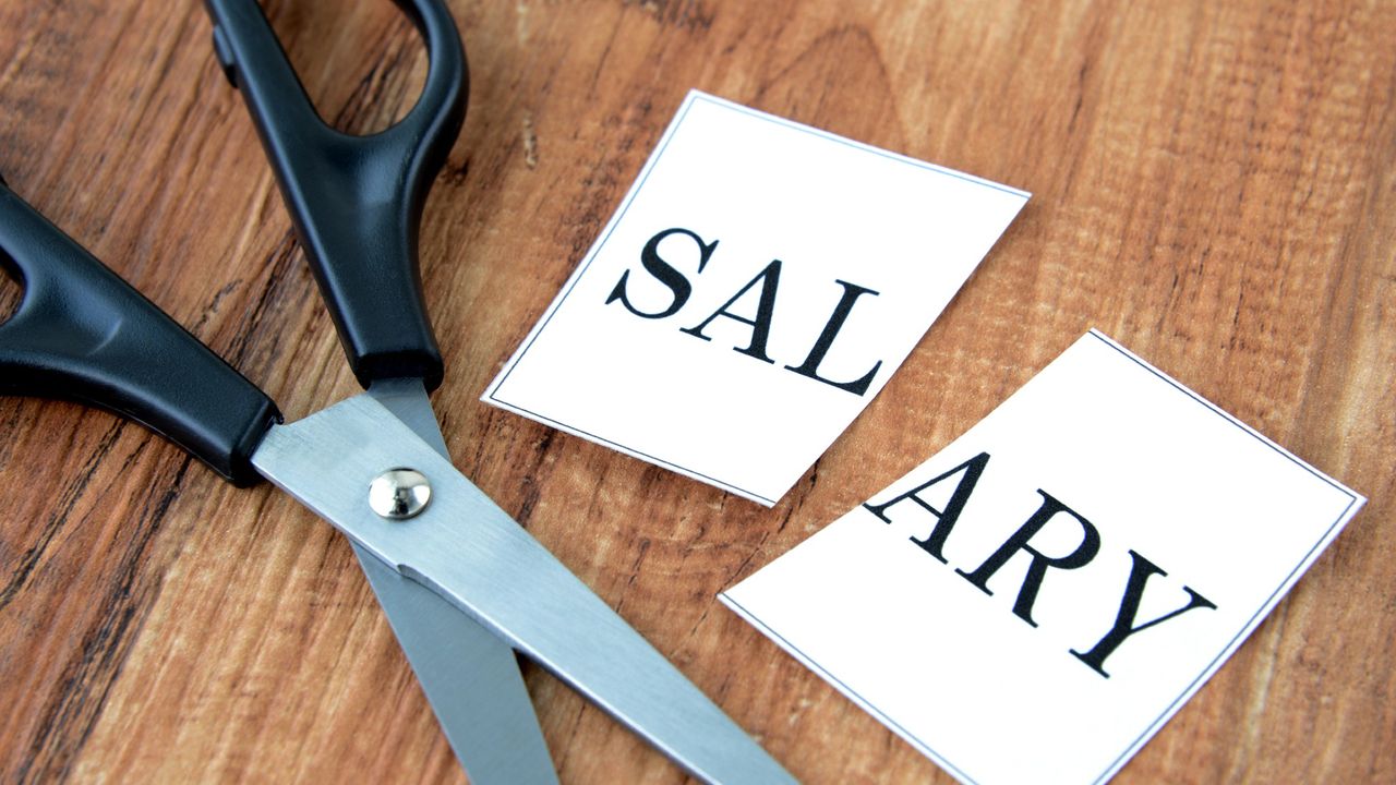 Scissors lying on a table next to a piece of paper that says &quot;salary,&quot; cut in half