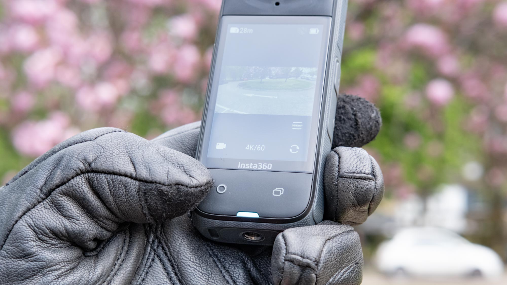 A photo of the Insta360 X4 being held in a leather gloved hand with a thumb about to press the record button.