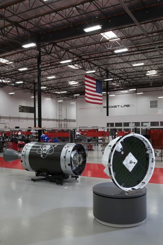 A Photon satellite (front) and an Electron rocket upper stage on the floor at a Rocket Lab facility.