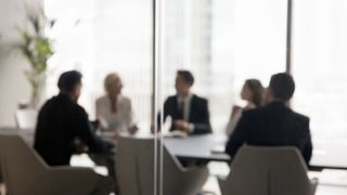 Group of businesspeople negotiating gathered in modern conference room, blurred silhouettes view, meeting behind closed glass doors. Business communication, workflow, decision-making, strategy sharing