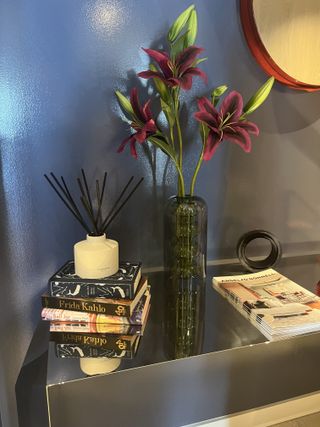 And entryway with blue walls, and a credenza with a stack of books, vase of flowers, and a Jo Malone candle