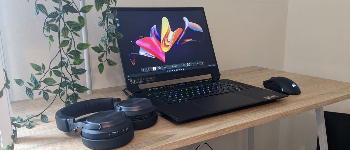 Corsair Voyager a1600 laptop open on a wooden desk with Corsair Virtuoso headset and Corsair Sabre Pro mouse.