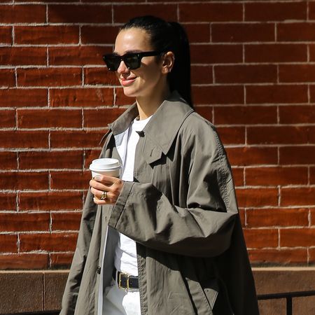 Dua Lipa wears white pants with an anti trend trench coat and black boots while walking with husband Callum Turner