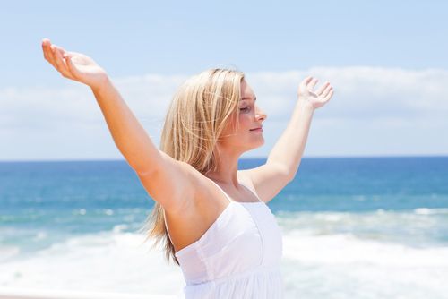 A woman walks on a beach with her arms raised and outstretched