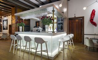 The restaurant's all white bar with wine glasses hanging from the top , bouquet of roses set on 2 ends of the bar and 7 white bar stools