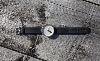 Watch with minimalist design and black strap lying on rough wood