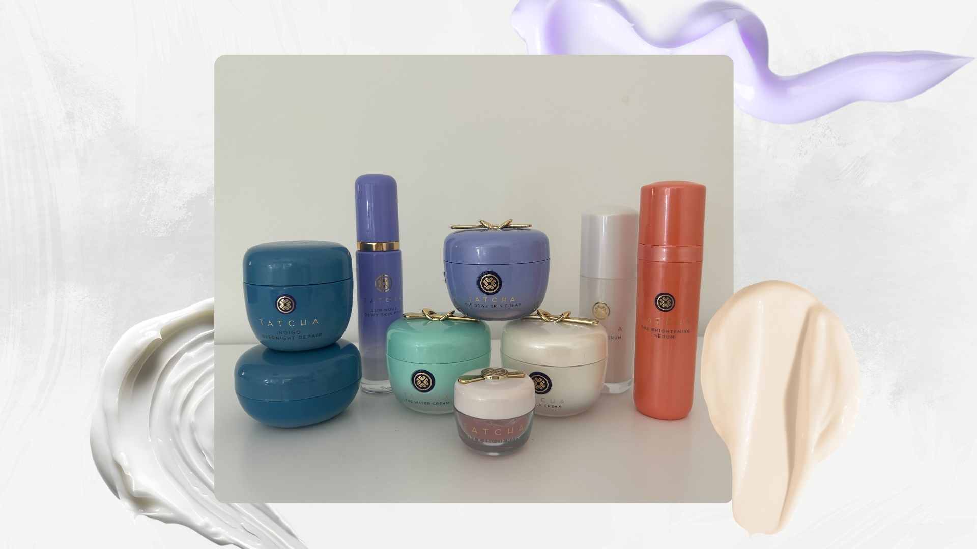 A picture showcasing nine of the Tatcha products tested for this guide, including the Dewy Cream and Kissu lip mask, arranged in a row in front of a white wall/ in a white and grey watercolour paint-style template with skincare cream swatches. 