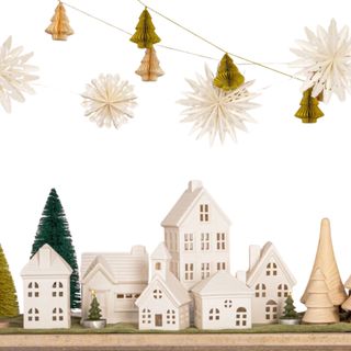 A white ceramic Christmas village with trees and paper garlands hanging above