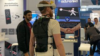 Actronika Skinetic vest, worn by a man who's also wearing a VR headset, in the middle of a busy event