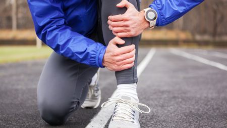 a runner holding their shin on a track