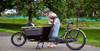 A women smiles at a baby in the cargo bucket of a black and yellow Raleigh Stride cargo bike in a park