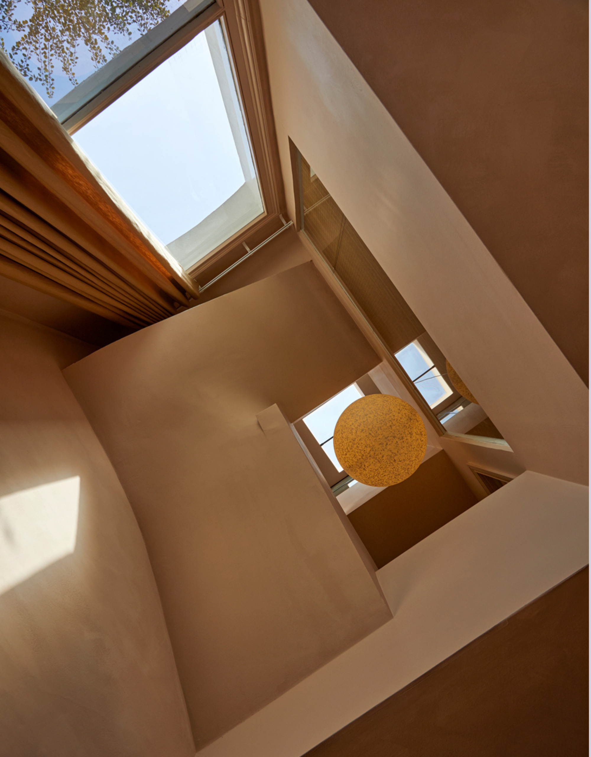 A globe pendant hung from the top of the triple height stairwell, painted in warm terracotta paint