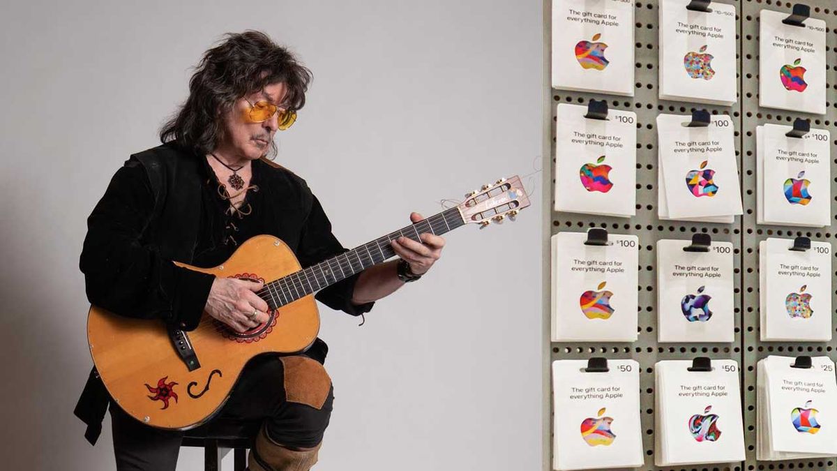 Ritchie Blackmore holding an acoustic guitar and some Apple gift cards on display 