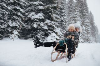 A happy couple sledging in front of a wintery forest backdrop.