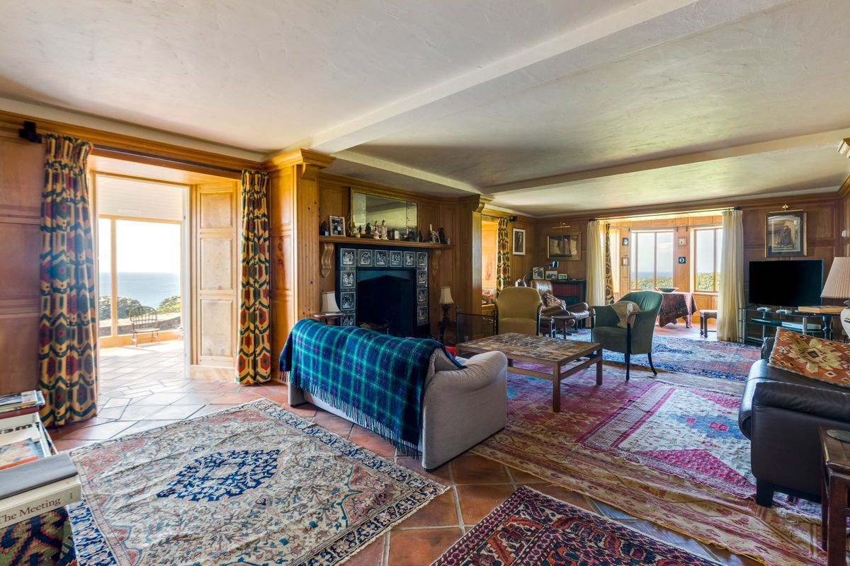 A living room with leather sofas surround a large fireplace and lead onto the conservatory
