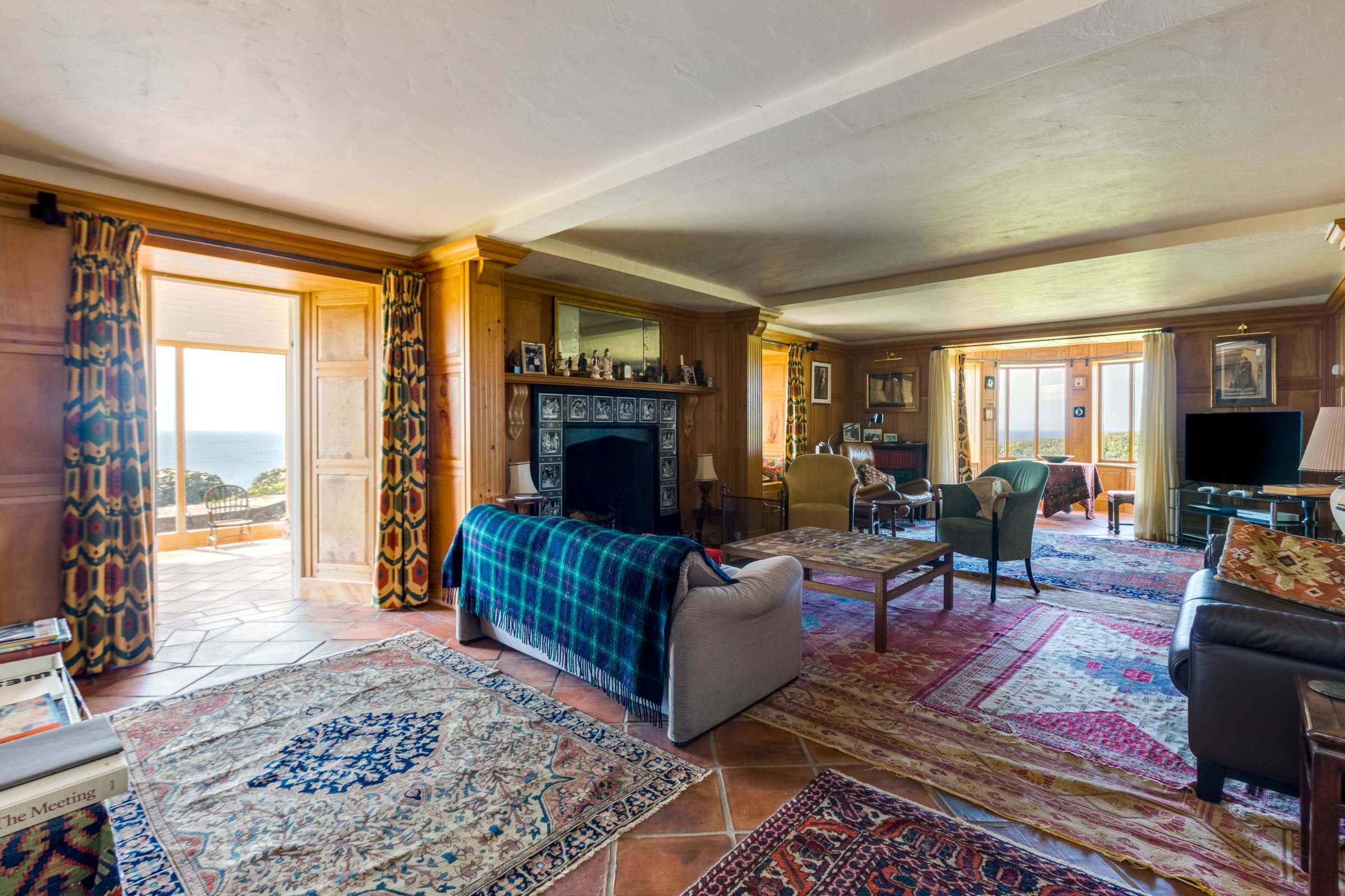 A living room with leather sofas surround a large fireplace and lead onto the conservatory