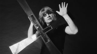 Ozzy Osbourne posed in a studio holding a large cross recreating the cover shot of the Blizzard Of Ozz album session