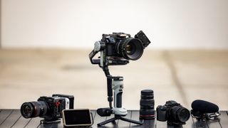 The Zhiyun Crane 4E on a table with various cameras and lenses