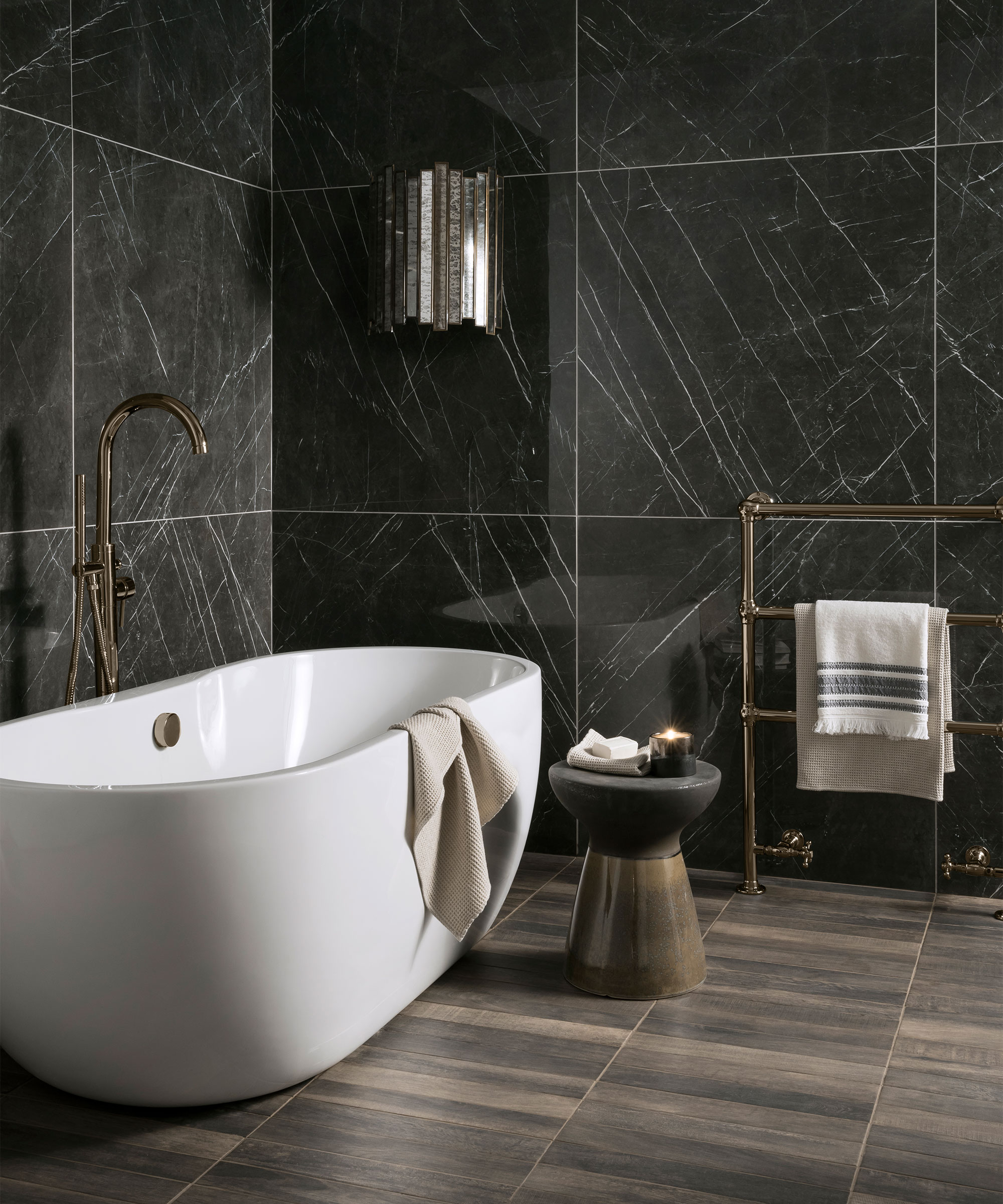 A bathroom with a white bath and large black wall tiles.