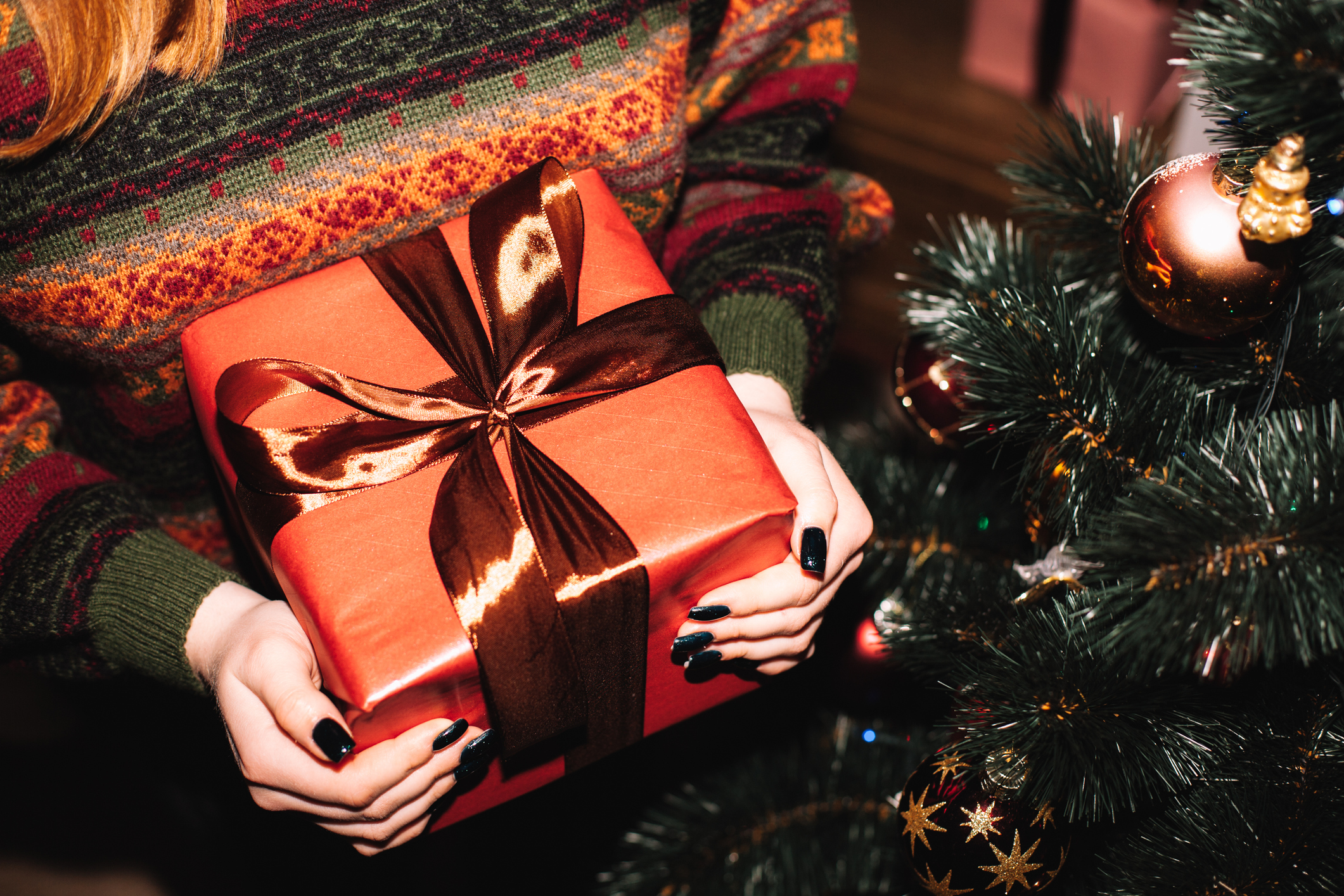 A close up of a person holding a red wrapped Christmas present with a red, satin bow.