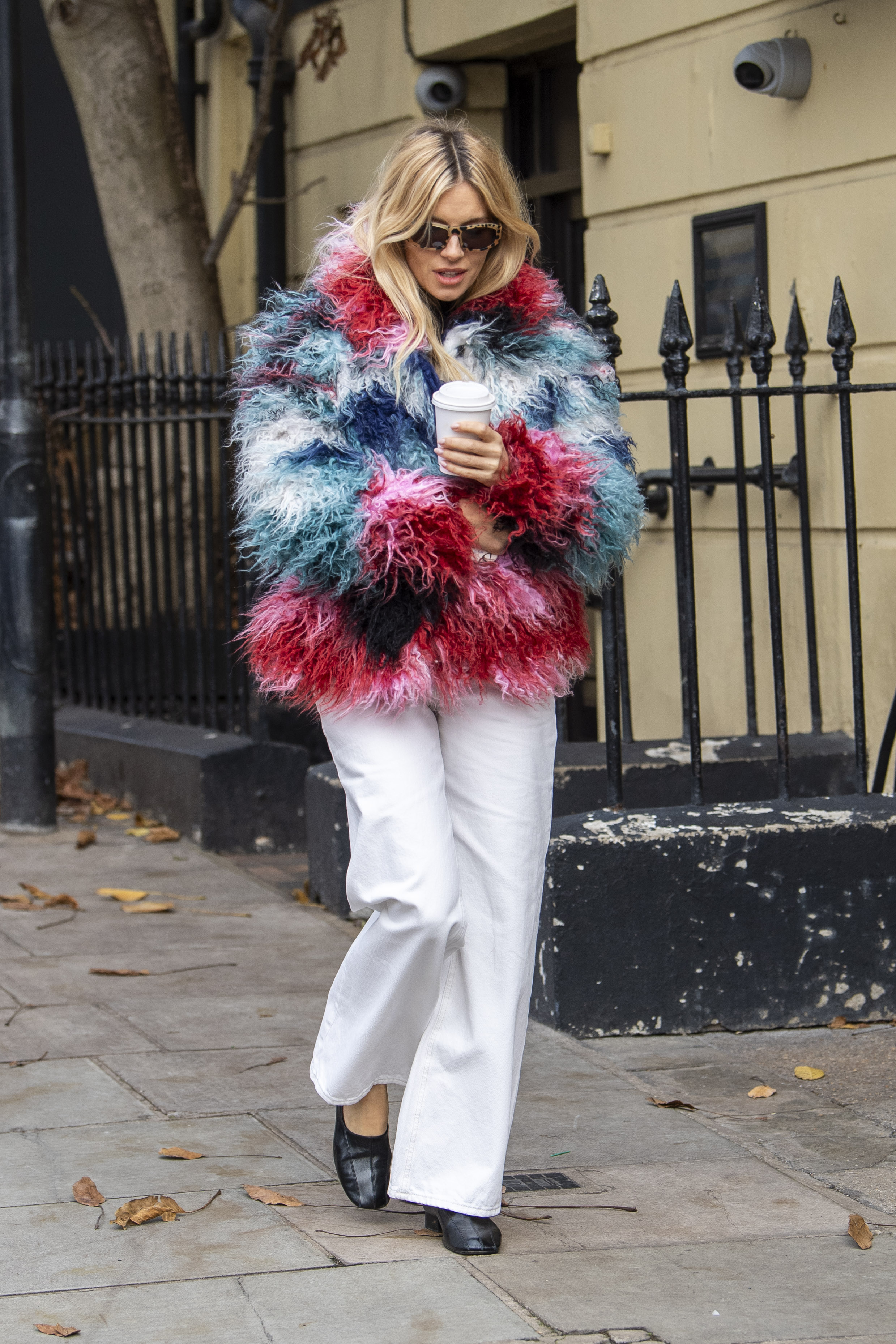 Sienna Miller walks down the street in London wearing a furry multi-coloured jacket from Desigual with white jeans and black leather ballet flats.