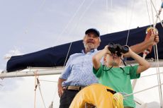 Boy and grandfather on sailboat looking through binoculars