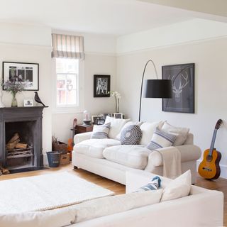 A white living room with sofas pulled away form the walls and a black fireplace and white sofa with blue cushions