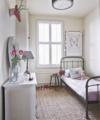 white bedroom with twin bed, woven rug and chest of drawers