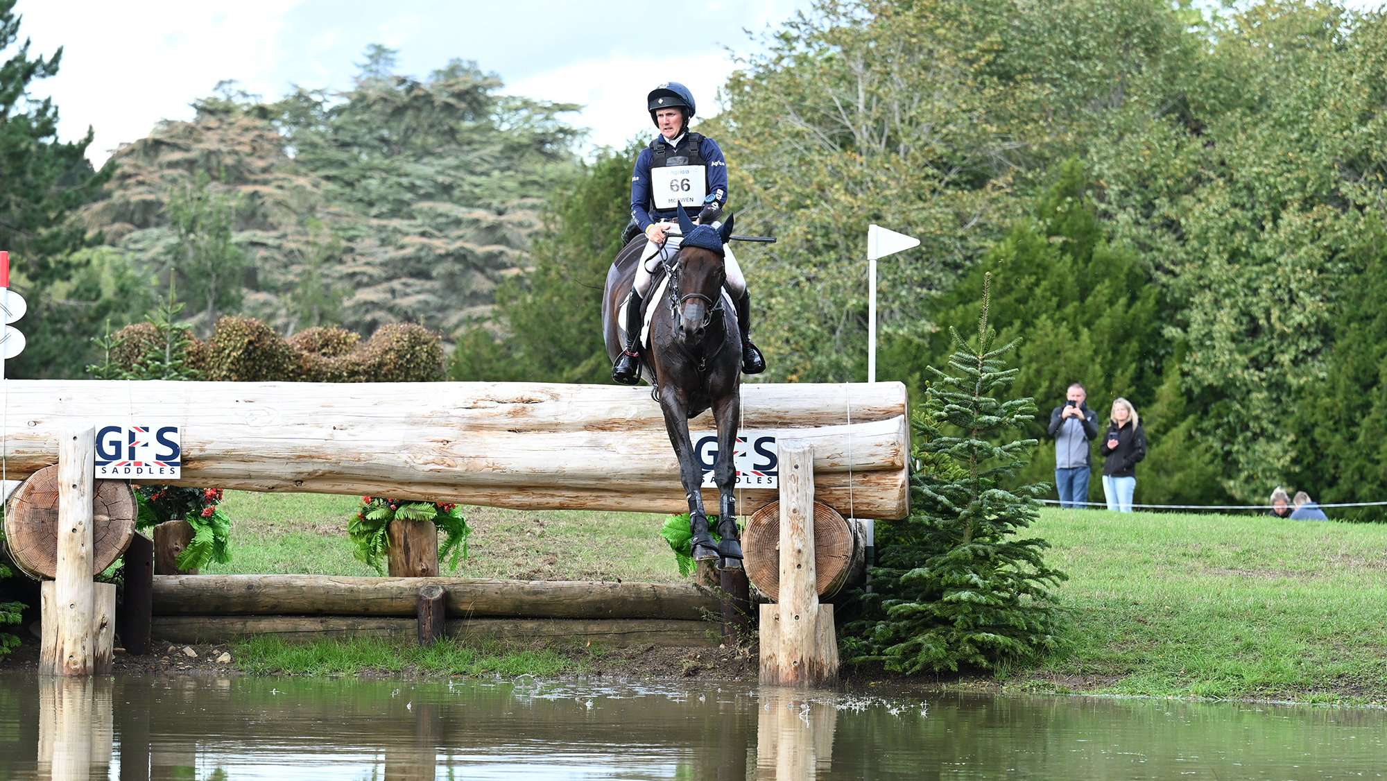 Tom McEwen, a rider in a blue top, rides dark bay horse Brookfield Quality over a log into water at Blenheim Horse Trials 2026