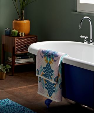 A colorful towel on the side of a deep green bath