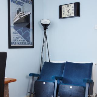 Cinema-style chairs against light blue-painted walls with a floor lamp and a clock
