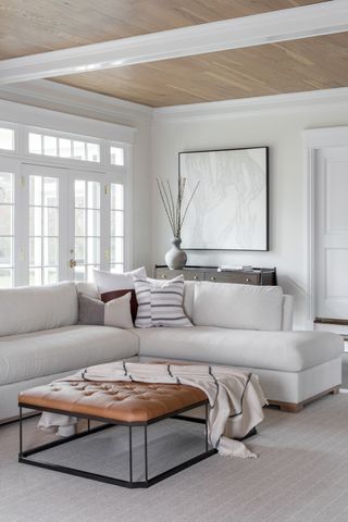 neutral living room with timber ceiling, white sofa, tan leather ottoman