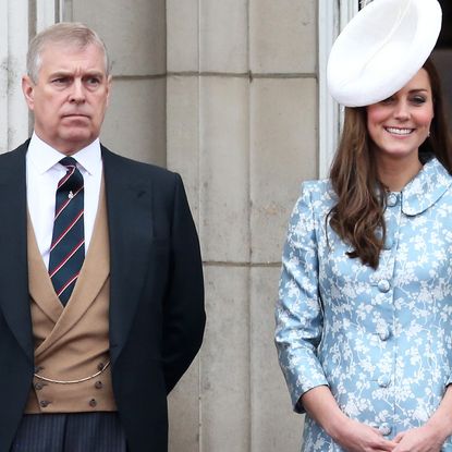 Prince Andrew wears a suit, waistcoat, and tie while stranding on the Buckingham Palace balcony next to Kate Middleton who wears a turquoise blue and white floral outfit and a large white hat