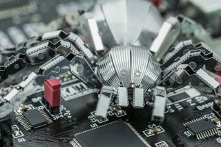 A metal spider standing on a printed circuit board