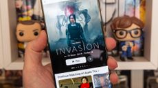 Apple TV+ running on an iPhone 16 Pro Max and shot in front of a bookshelf with Funko Pops