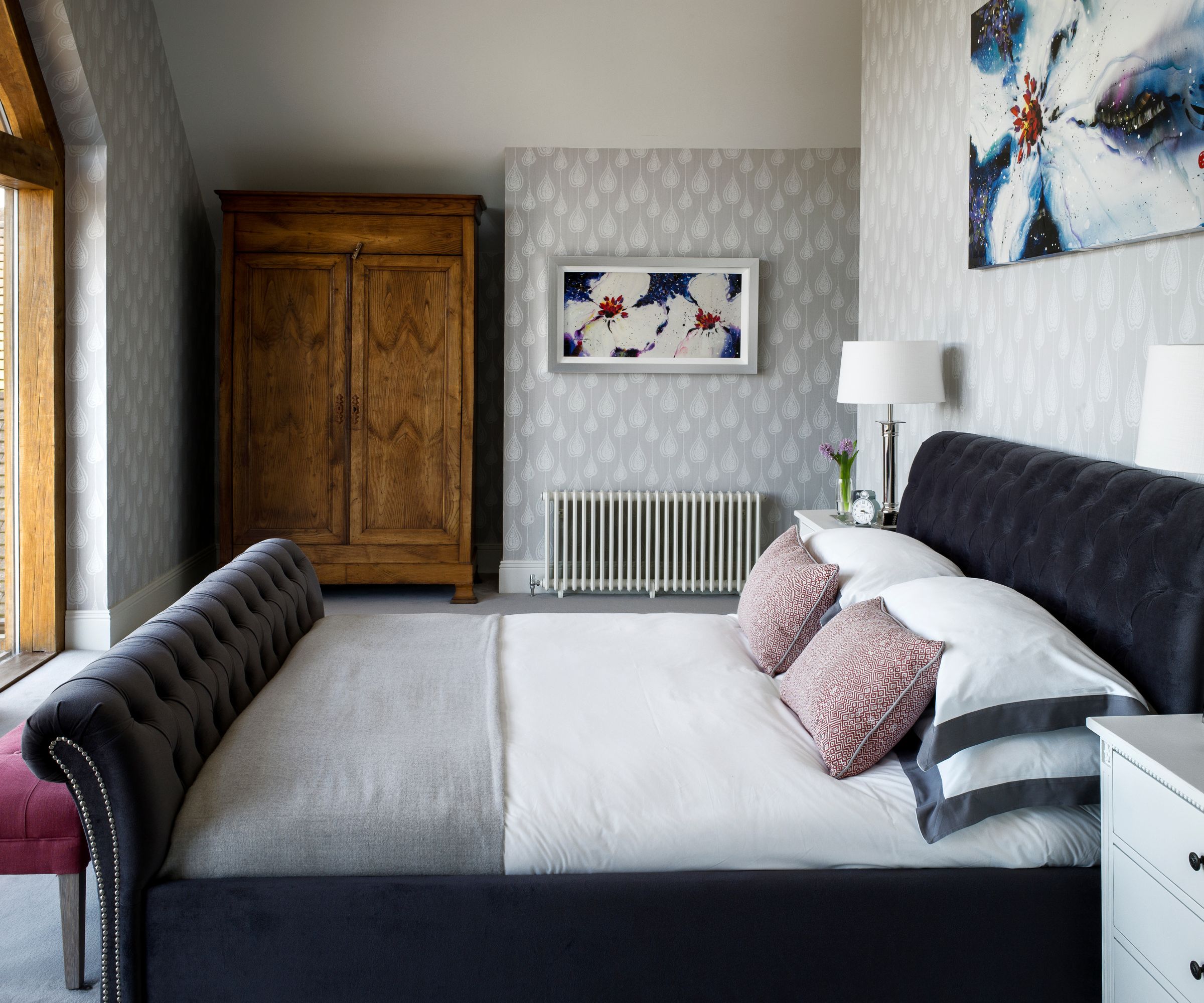 Grey bedroom with velvet bed frame, grey carpet, grey wallpaper and pink pillows