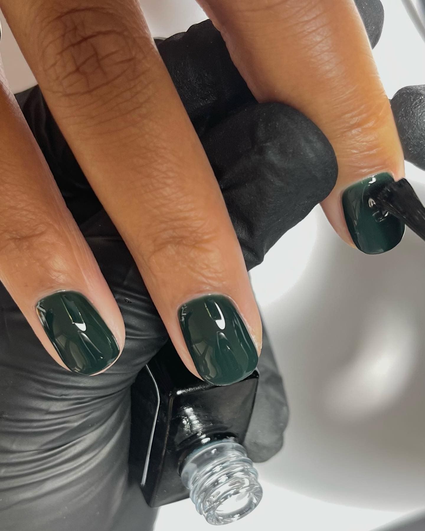 A close up photo of a nail tech painting short nails with dark green polish