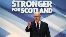 John Swinney, the new leader of the SNP, delivers a speech in front of a background that says 'stronger for Scotland'