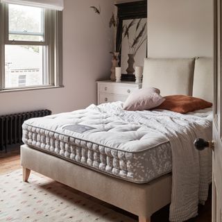 A mattress on a beige upholstered bed in a pale cream bedroom