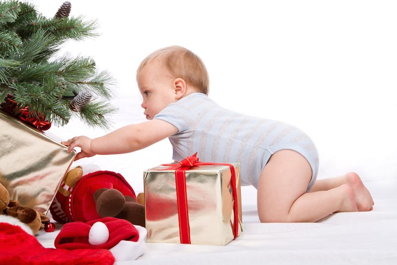 A baby reaches for a present beneath a Christmas tree