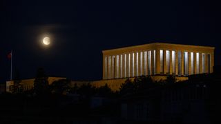 partly eclipse moon on the left with a large building on the right with many columns.