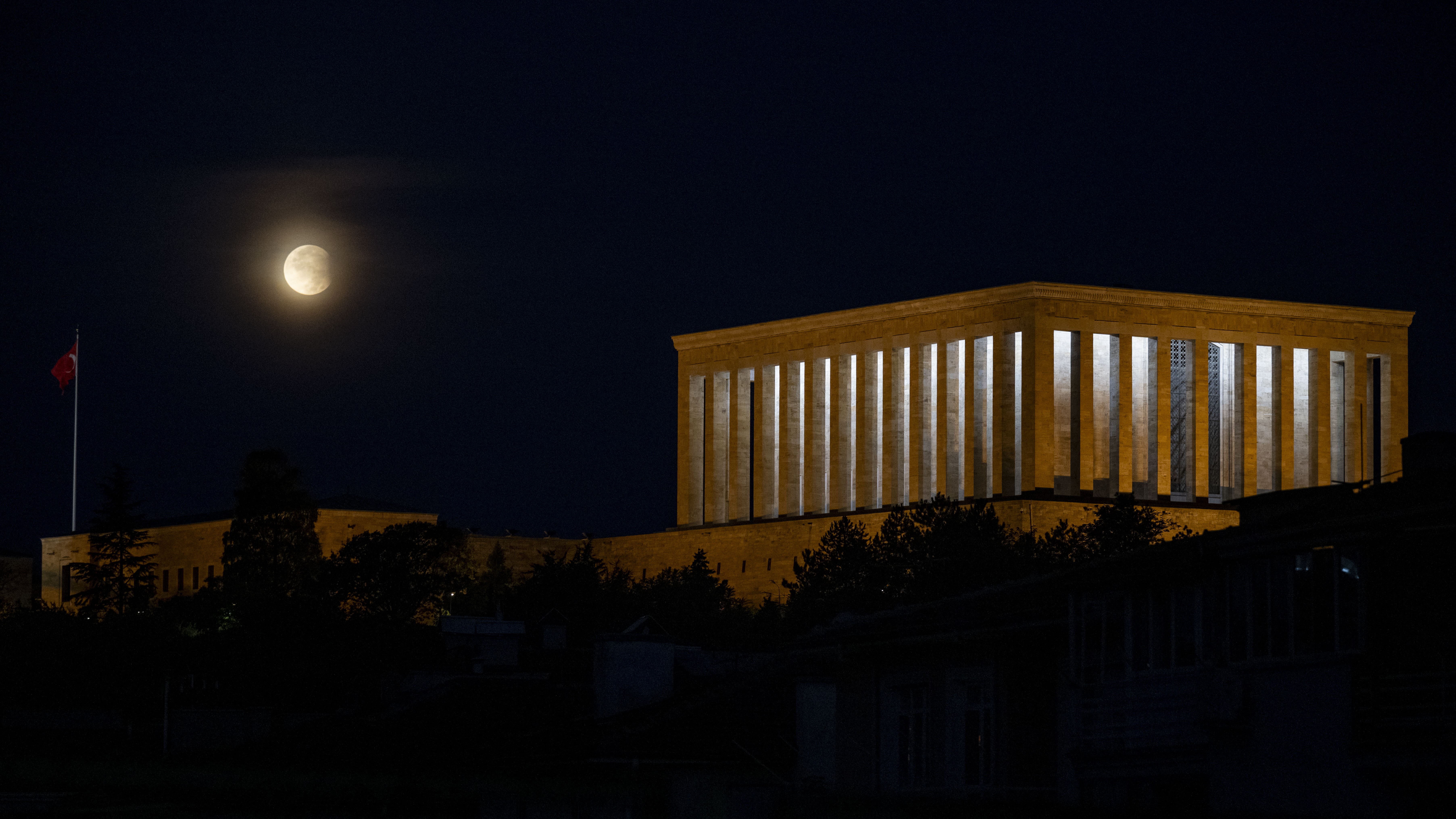 partly eclipse moon on the left with a large building on the right with many columns.