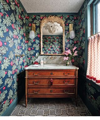 wood washstand with marble top and patterned wallpaper and gold edged mirror