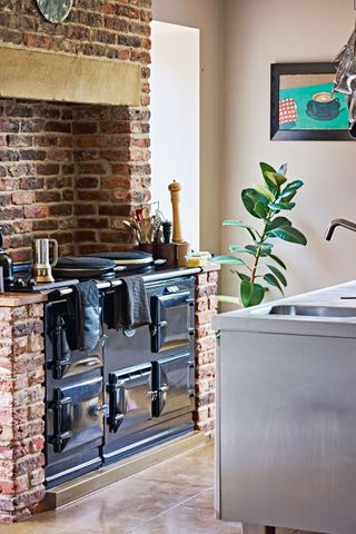 kitchen with black range cooker and exposed brick surround and steel topped island