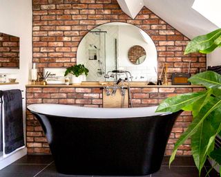Rustic-industrial bathroom with worn brick effect wall tiled and black freestanding bathtub