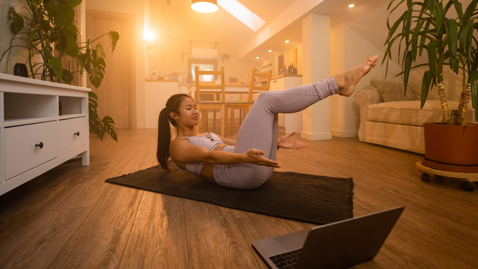 Woman exercising on an exercise mat at home, an open laptop is on the floor in front of her