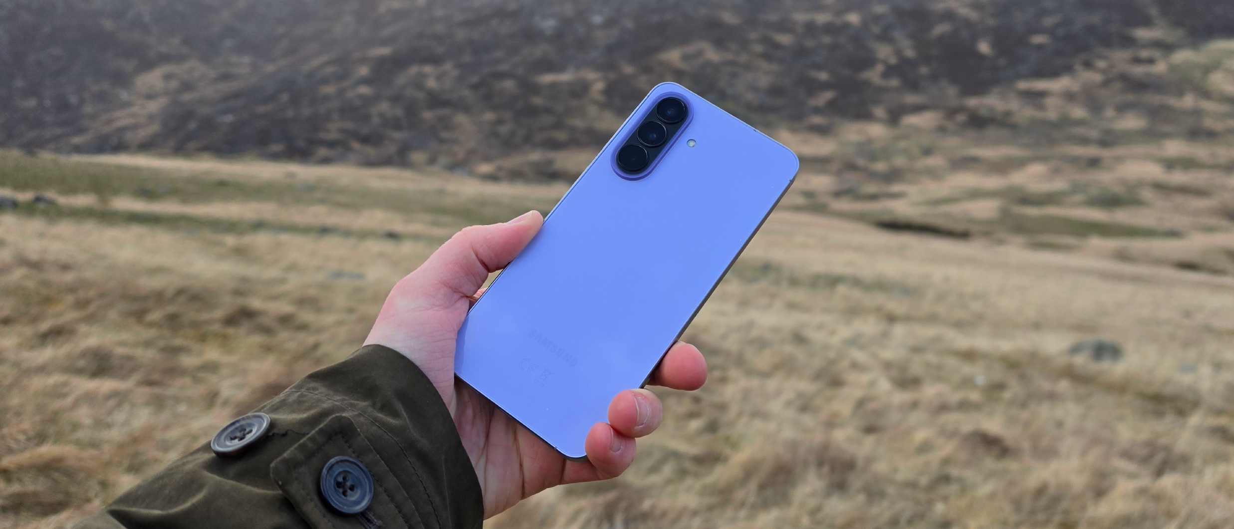 The Samsung Galaxy A57 being held over a field, showing its back.