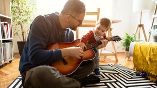 Father shows his baby how to play guitar